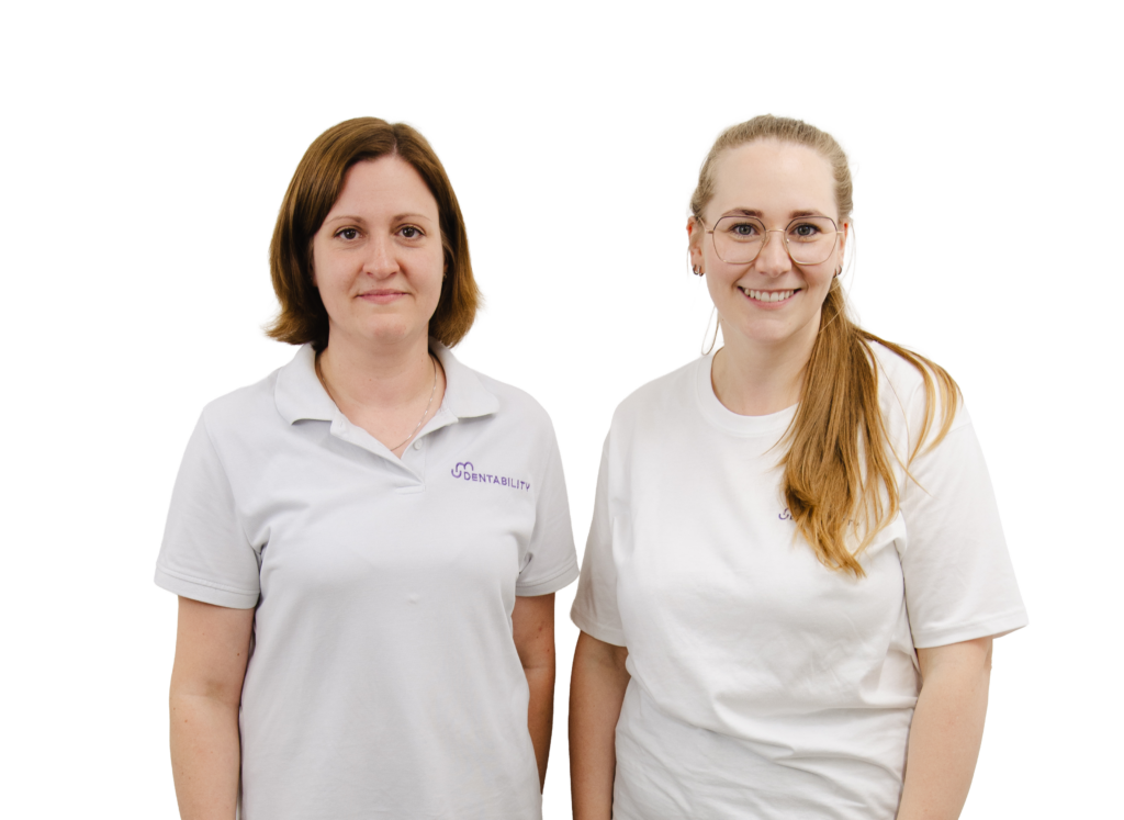 Zwei Dentability-Teammitglieder in weißen Poloshirts, lächelnd in der Zahnarztpraxis